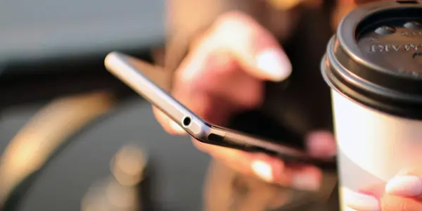time management skills - person checking phone with coffee in other hand